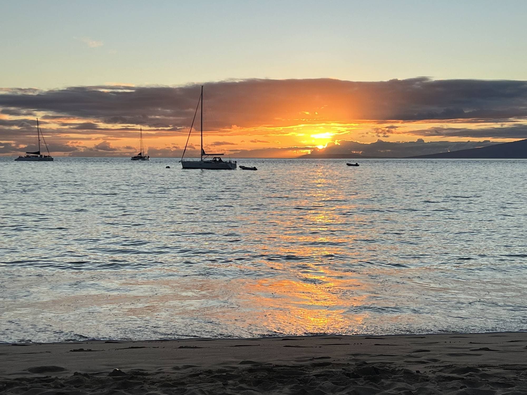 Sailboats anchored off a Maui beach at sunset